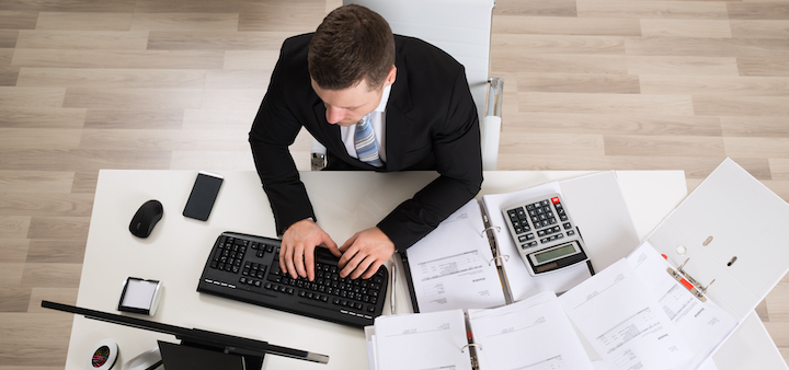 High angle view of businessman analyzing documents at computer desk in office
